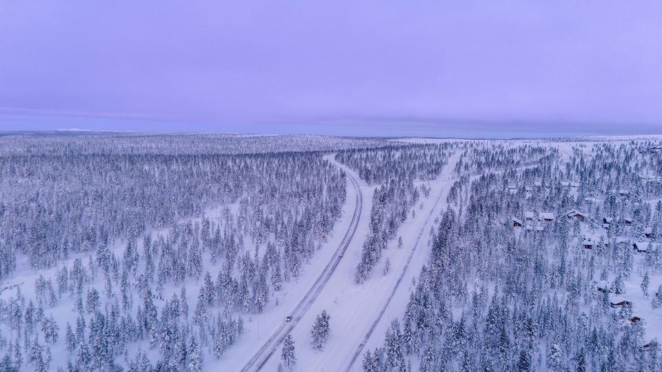 An aerial view of a road winding through snowy Lapland forest