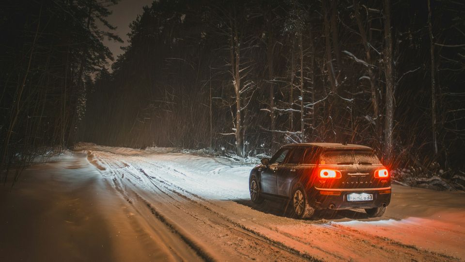 A car with red tail lights on a snowy forest road at night
