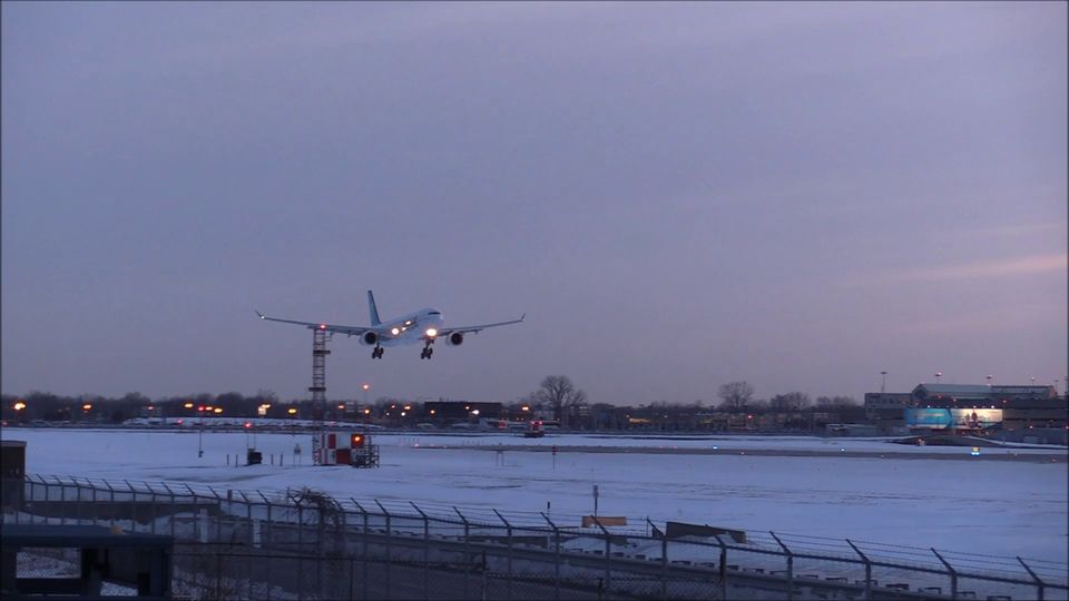 A passenger jet landing on a snowy airport runway under a pink winter dusk sky (video)