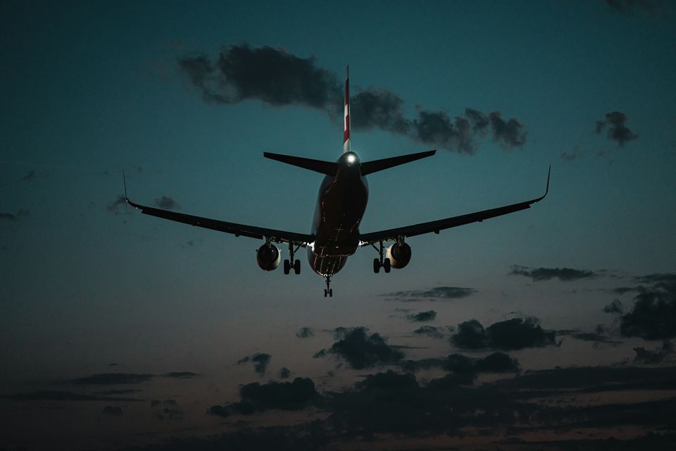 A passenger jet on final approach, wheels down, against a teal dusk sky