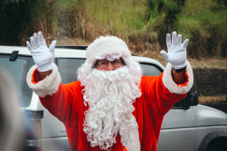 Santa Claus waving both hands in front of a white car