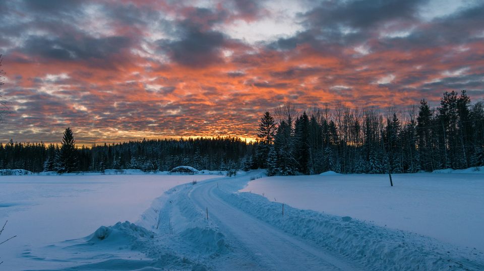 A snowy road under a fiery pink and orange winter sunset