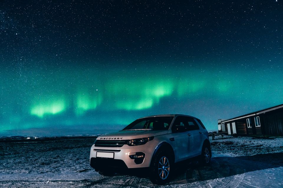 An SUV parked on a snowy plain beneath green Northern Lights